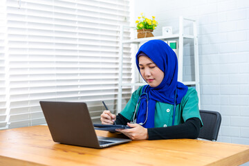 Female Muslim Islamic doctor working in hospital modern office exam checkup clinic room, wearing scrub outfit and stethoscope happy smiling, multi ethnicity working in the medical healthcare industry. - obrazy, fototapety, plakaty