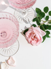 A pink rose and two glasses with rose drink on a white table, shot from above