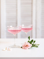 Two glasses with pink rose drinks and a pink rose on a white table