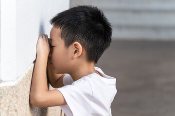The cute Asian little boy is playing hide and seek with the funny moments. Asian kid crying on the wall. Child playing hide-and-seek hiding face.