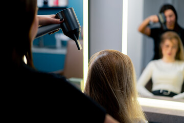 the hairdresser dries the client's wet hair with a hair dryer in the beauty salon, a care procedure