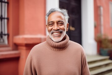 Portrait of a smiling indian man in his 70s dressed in a warm wool sweater against a solid pastel...