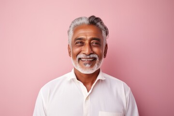 Portrait of a blissful indian man in his 70s wearing a simple cotton shirt against a solid pastel...