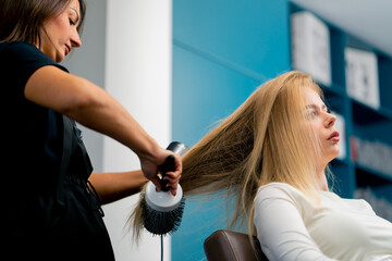 close-up hairdresser dries the client's hair with a hair dryer with a comb in a beauty salon styling