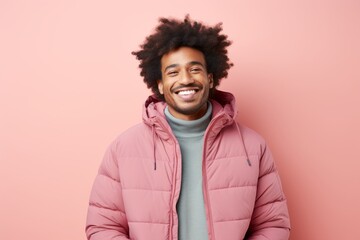 Portrait of a grinning afro-american man in his 20s donning a durable down jacket against a solid...