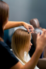 Fototapeta premium hairdresser sprays hairspray on client's hair after styling care procedure in beauty salon