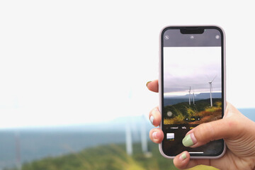 Woman hand using smartphone taking photo of windmill landscape view. Clean energy concept, wind power