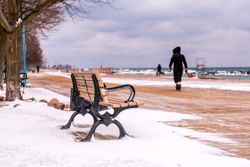 park bench on snowy winter day Kew Beach wooden boardwalk in Toronto's Beaches neigbourhood with dog walkers  (out of focus) in background room for text