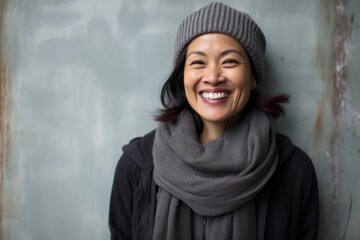 Portrait of a joyful asian woman in her 40s donning a warm wool beanie against a bare concrete or plaster wall. AI Generation - obrazy, fototapety, plakaty