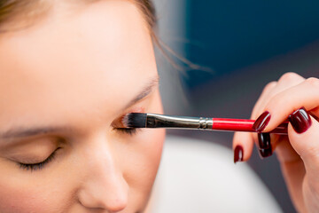 close-up of a make-up artist applying eyeshadow with a brush to a client's face in a beauty salon