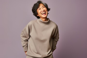 Obraz premium Portrait of a jovial asian woman in her 60s dressed in a comfy fleece pullover against a blank studio backdrop. AI Generation