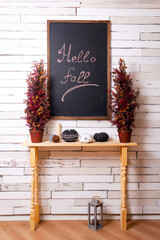 a black chalkboard with a table on the background of a wooden wall. a drawing board with the inscription "hello fall" in the photo studio. Autumn photo zone in the photo salon
