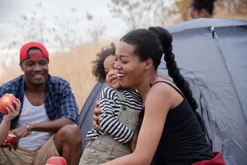 Happy African American family with adorable children enjoy weekend vacation camping outdoors in countryside, cheerful children laughing running around father holding apple fruit, bonding relationship