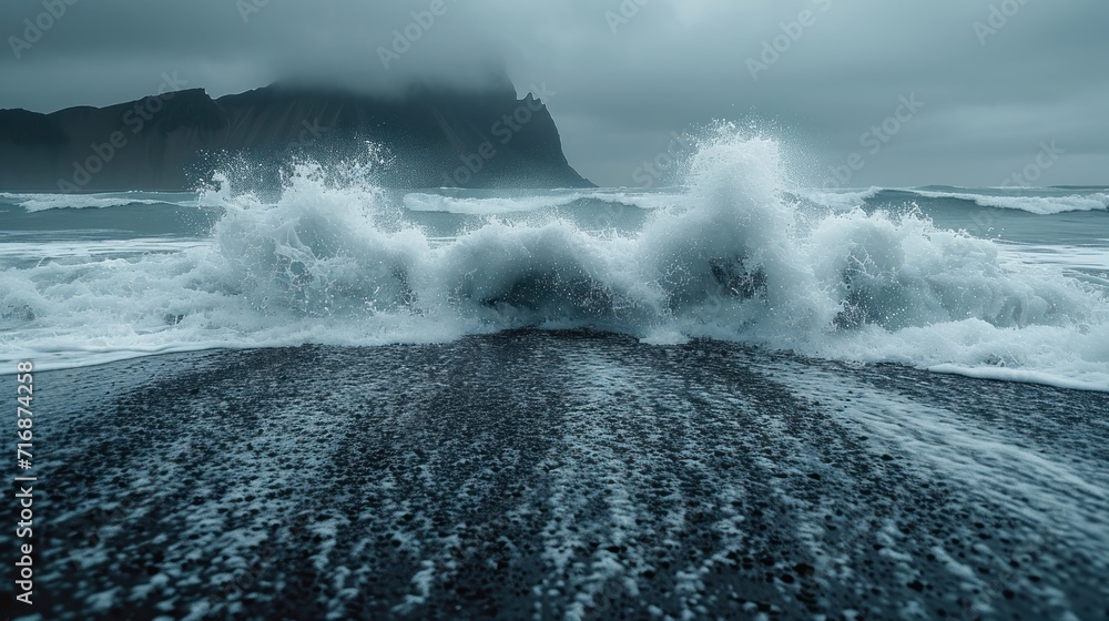Poster a large wave crashes into the shore of a beach on an overcast day with a rock outcropping in the for