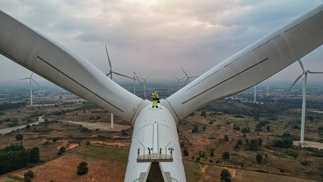 Windmill engineer wearing PPE standing on wind turbine.  engineer feel success after good work. He standing a top of windmill.