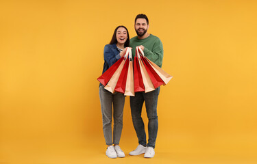 Happy couple with shopping bags on orange background