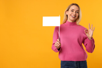 Fototapeta na wymiar Happy woman with blank white flag showing OK gesture on orange background. Mockup for design