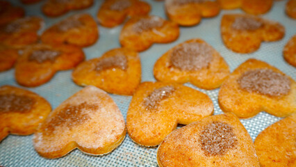 On a silicone mat there are a lot of gluten-free cottage cheese cookies in the shape of hearts sprinkled with cinnamon and sugar after baking in the oven. side view