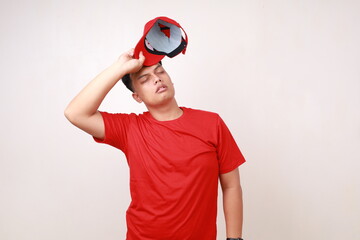 Tired young asian courier standing while holding head against white background