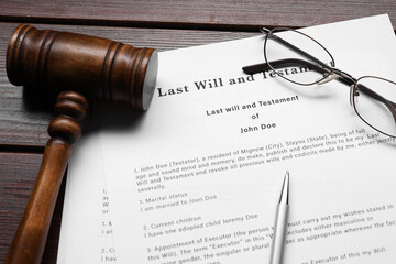 Last Will and Testament, glasses, pen and gavel on wooden table, closeup