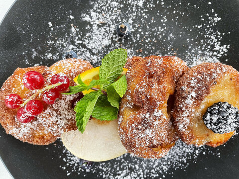 Apple Fritters on a dark plate with sugar and fruits