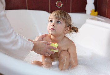Mother washing her little daughter with sponge in bathtub, closeup