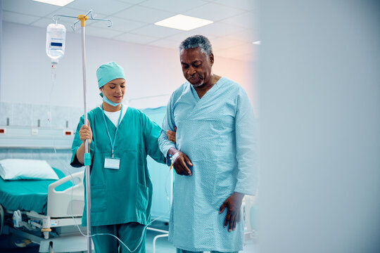 Caring nurse assisting black senior man in his recovery after surgery at medical clinic.