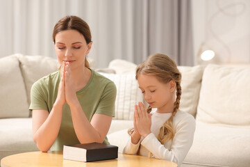 Girl and her godparent praying over Bible together at table indoors
