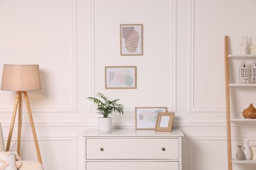Picture frames hanging on white wall and chest of drawers at home