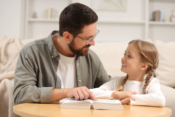 Girl and her godparent reading Bible together at table in room