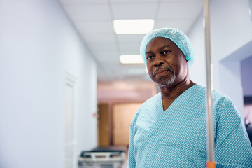 Black senior man with IV drip in hospital ward looking at camera.