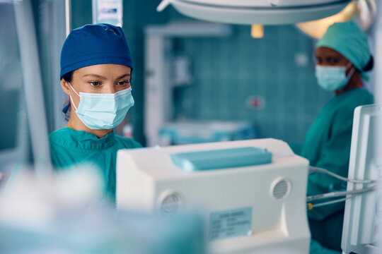 Female anesthesiologist looking at screen while monitoring patient's vitals in operating room during surgery.