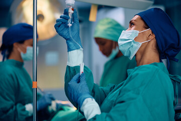 Female anesthesiologist monitoring IV drip during surgery in operating room.