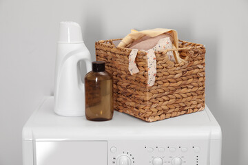 Baby clothes in wicker basket and laundry detergents on washing machine near light wall