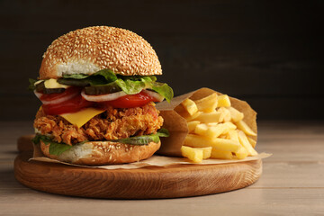 Delicious burger with crispy chicken patty and french fries on wooden table
