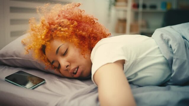 Young curly-haired woman sleeping in bed till late morning, procrastination
