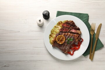 Delicious grilled beef steak and vegetables served on light wooden table, top view. Space for text
