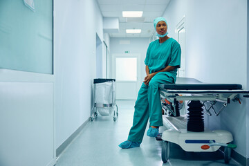 Pensive black female surgeon on break in hospital hallway.