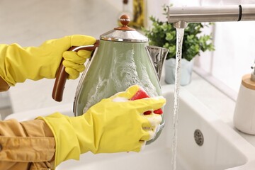 Woman washing electric kettle with sponge at sink in kitchen, closeup