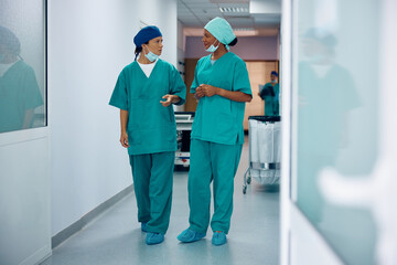 Black surgeon and her female colleague communicating while walking through hospital hallway.