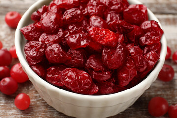 Tasty dried cranberries in bowl and fresh ones on rustic wooden table, closeup
