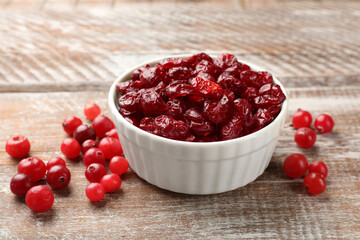 Tasty dried cranberries in bowl and fresh ones on rustic wooden table, closeup