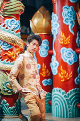 Fototapeta na wymiar Portrait of young Asian man in traditional male Cheongsam Chinese dress on Chinese new year day isolated on Chinese shrine background, happy Chinese new year concept.Young man celebrating festival