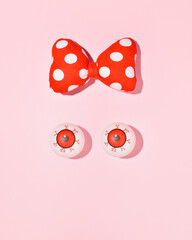 Table tennis balls creatively painted as eyes and big polka dots hair bow, minimalistic female face, retro fashion trend.