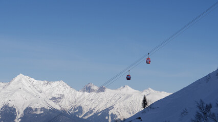 Ski resort on sunny winter day. Ski lift funicular cab lifts skiers and snowboarders up mountain...