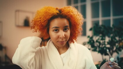 Young African American woman applying moisturizing serum on her dry curly hair - Powered by Adobe