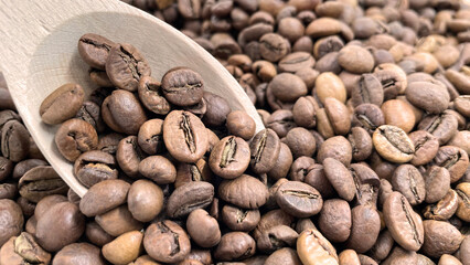 Top view of a pile of scattered aromatic roasted brown coffee beans with a wooden scoop. Coffee beans in a wooden spoon. Fragrant coffee, coffee drinks.
