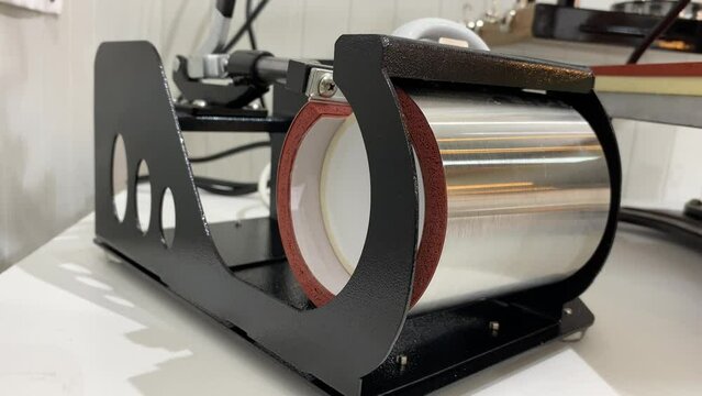 Male hand making a personalised white glass coffee mug with heat press printing machine.