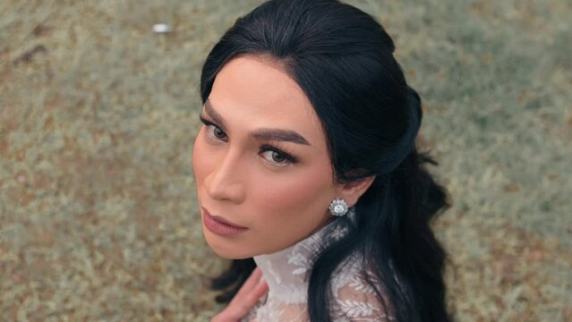 Elegant woman with dramatic makeup posing outdoors, wearing a lace dress and earrings.