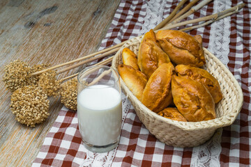 Pies with filling in a wicker basket on a wooden board, next to there is a glass of milk and dried plants. Rustic motif Top view and copy space.Pirozhki or piroshki.Dough products